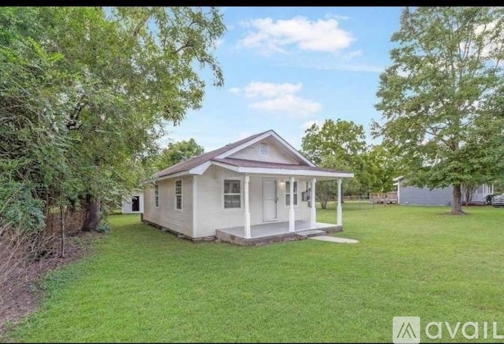 A small white house with a porch is surrounded by green grass and trees.