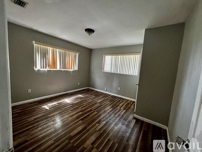 A room with wooden floors and two windows with blinds.
