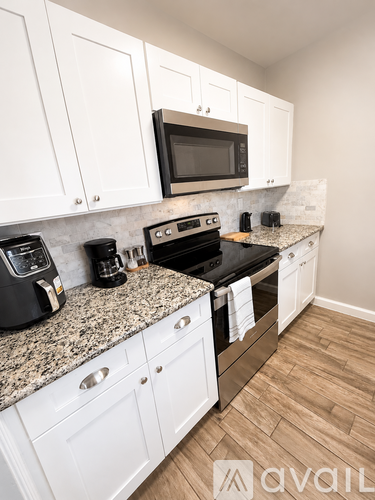 A room with a ceiling fan and a kitchen area with a refrigerator and a sink.