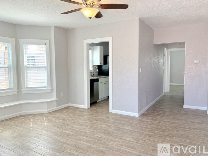 A room with a ceiling fan and a kitchen area with a refrigerator and a sink.