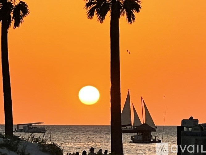 A sunset scene with palm trees and a sailboat.