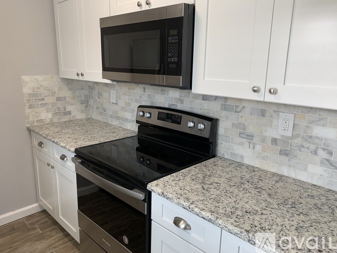 A kitchen with a black microwave above a stove and white cabinets.