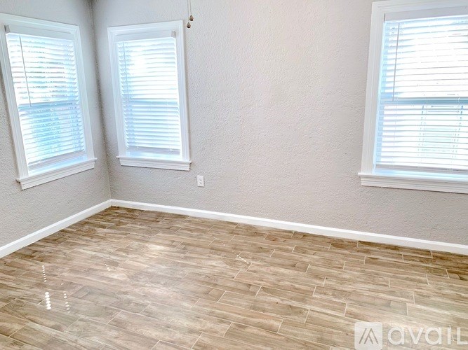 A room with light wood flooring and two windows with blinds.