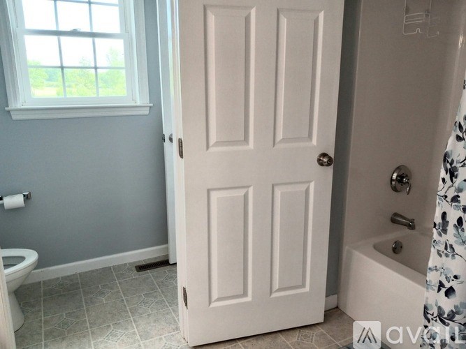 A white door is in a bathroom with a toilet and tub.