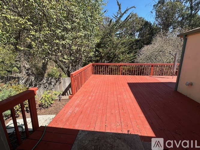 A red wooden deck with a railing and trees in the background.