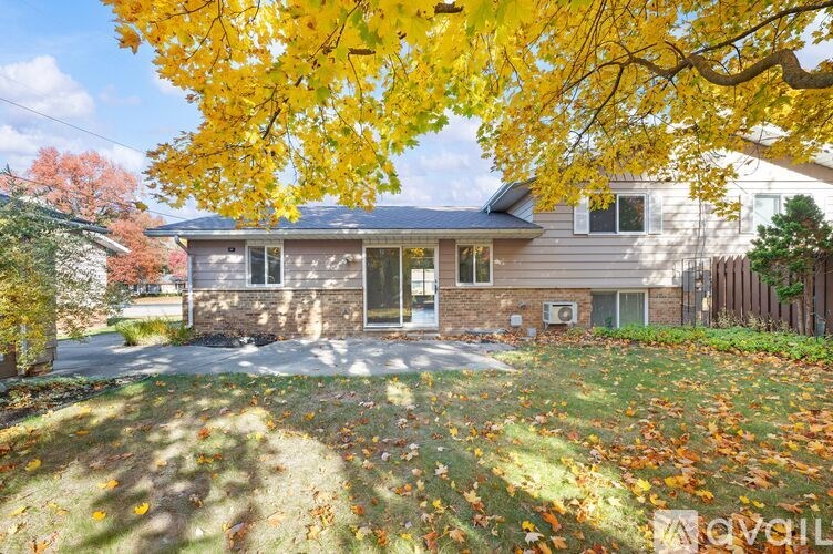 A house with a driveway and a tree with yellow leaves in front.