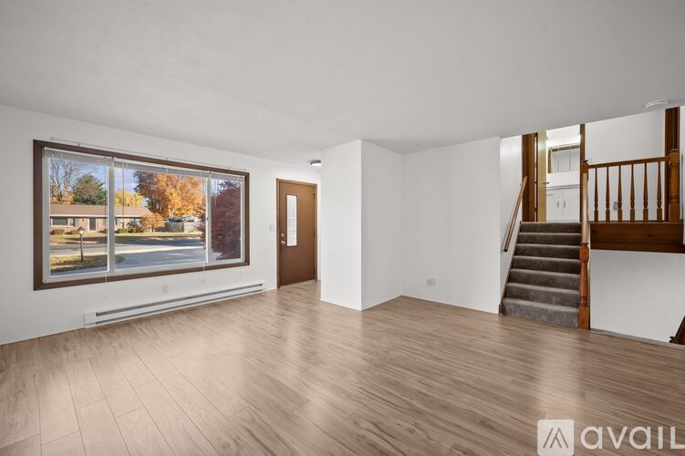 A spacious room with wooden flooring and a staircase leading to another room.
