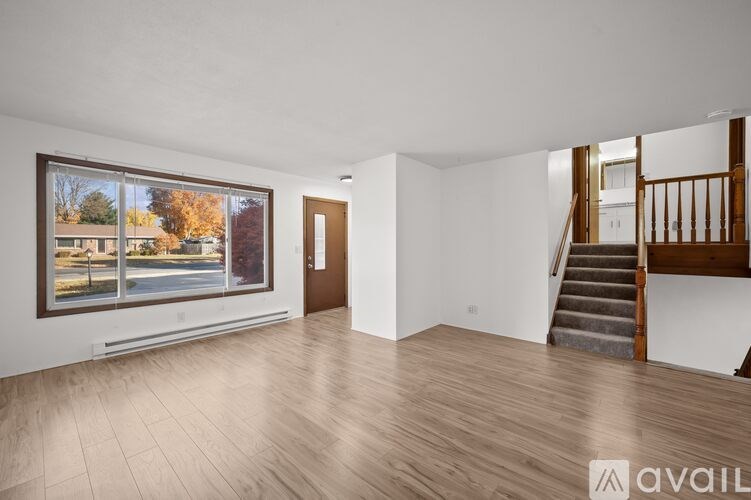 A spacious room with wooden flooring and a staircase leading to another room.