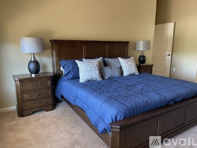 A bed with a blue comforter and matching pillows is flanked by two lamps on a nightstand.