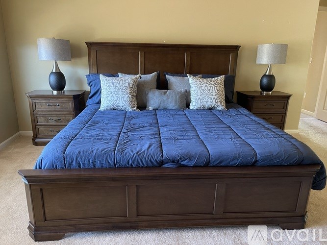 A bed with a blue comforter and matching pillows is flanked by two nightstands with lamps on them.