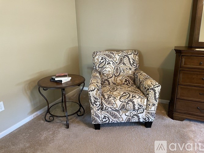 A chair with a patterned cover sits in a room with a small table and a dresser.