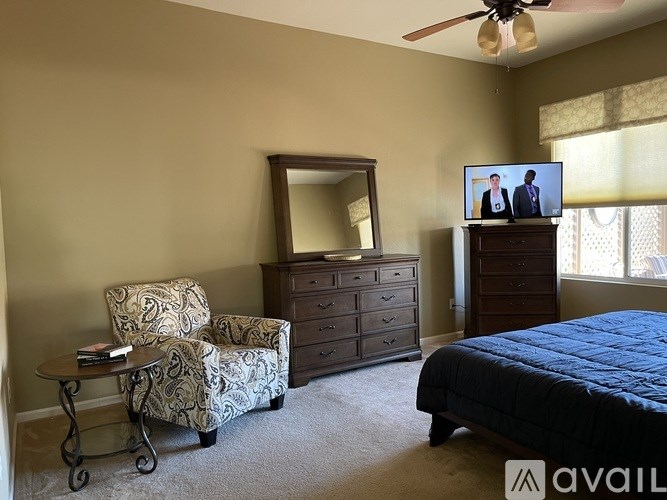 A bedroom with a bed, dresser, chair, and a television on top of the dresser.