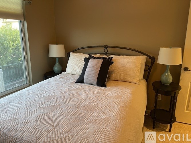 A bed with a white comforter and a black headboard with two pillows and two lamps.