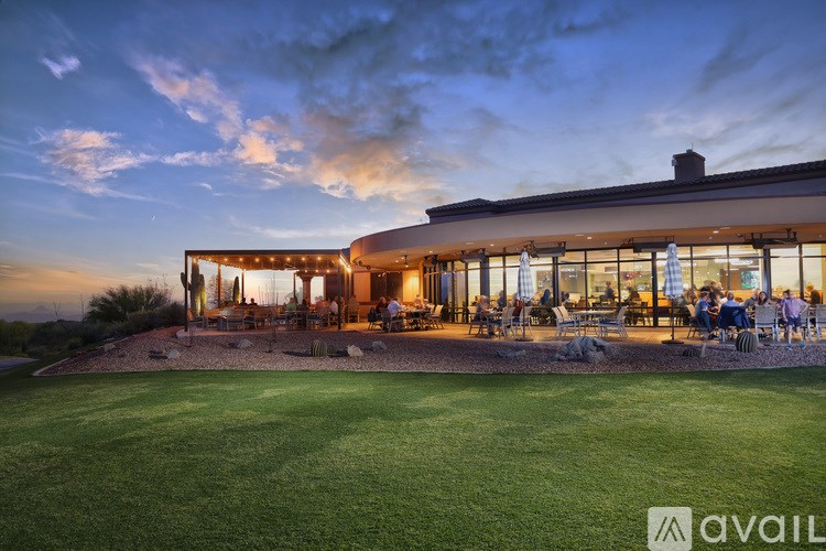 A modern building with a large glass facade and people sitting outside at night.