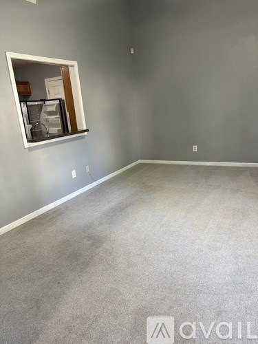 A room with grey carpet and a grey wall with a window.