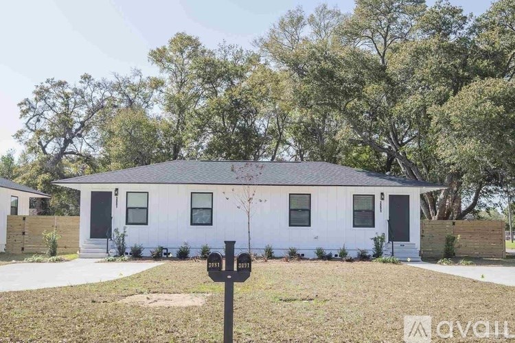 A white house with a black door and windows is surrounded by trees.