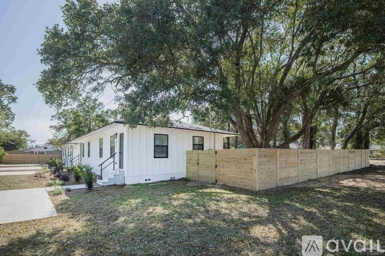 A white house with a wooden fence and trees in the background.