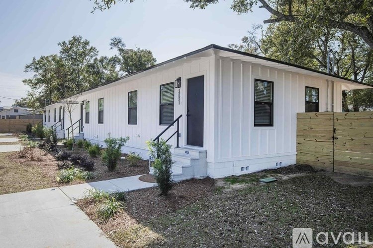 A white house with a black door and windows is surrounded by a garden.