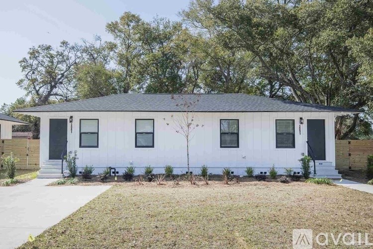 A white house with a black roof and a tree in front.
