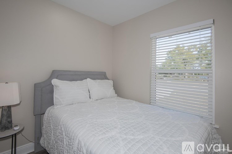 A bedroom with a bed, nightstand, and window with blinds.