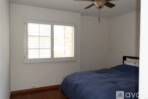 A bedroom with a bed, a window with blinds, and a ceiling fan.