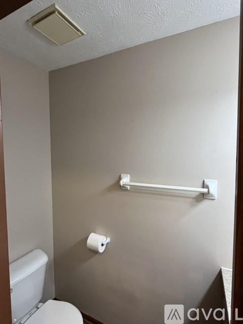A white toilet is in a small bathroom with a towel bar and toilet paper.