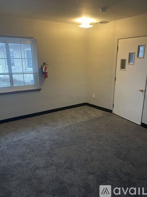 A room with a white door, a window with blinds, and a fire extinguisher on the wall.