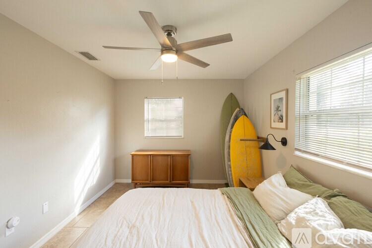 A bedroom with a bed, a surfboard, and a ceiling fan.