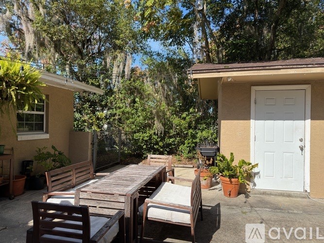 A patio with a table and chairs is surrounded by greenery.