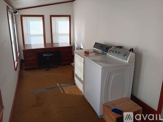A small room with a washing machine and a wooden stool.