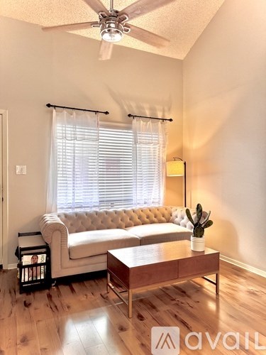 A living room with a white sofa, a wooden coffee table, and a ceiling fan.