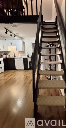 A staircase with a beige carpeted runner and wooden steps leads to a kitchen area.