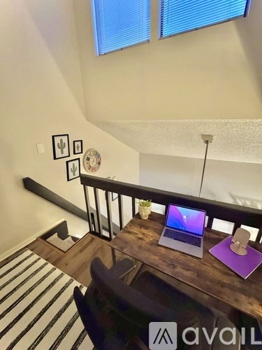 A laptop is on a wooden desk with a purple mouse pad.