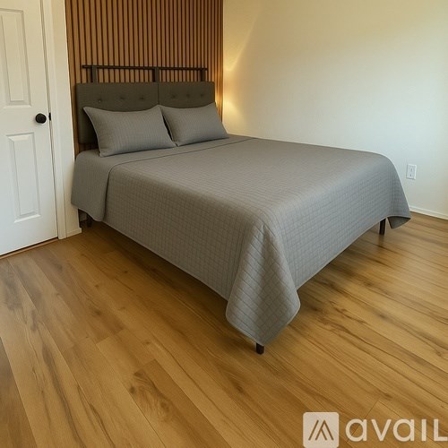 A bed with a grey bedspread and two pillows is in a room with wooden flooring.