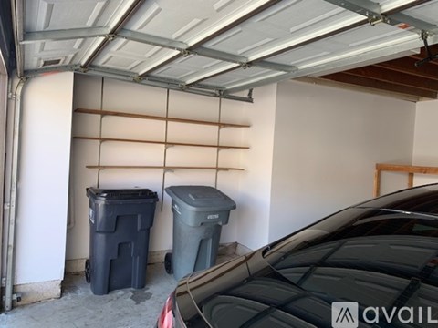 A car is parked in a garage with two trash bins.