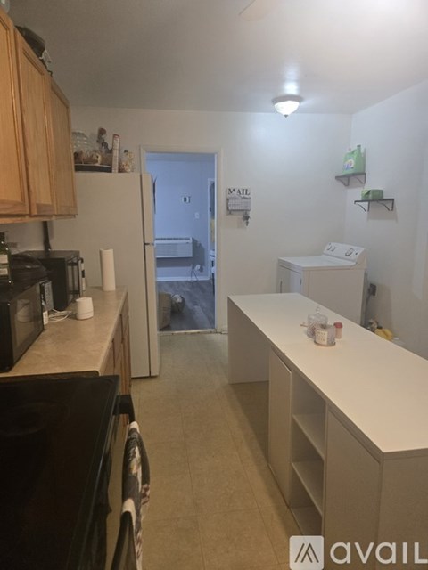 A kitchen with a black fridge and microwave, a white washing machine, and a white counter with a few items on it.