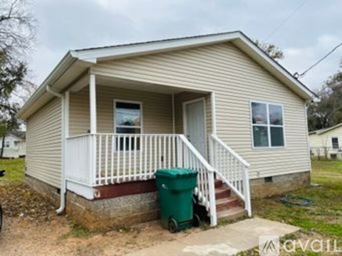 A small house with a porch and a green trash can in front.