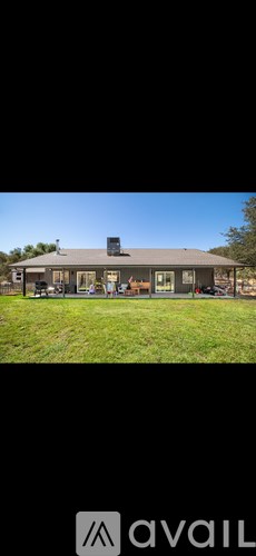 A house with a dark roof and a chimney is surrounded by a grassy lawn.