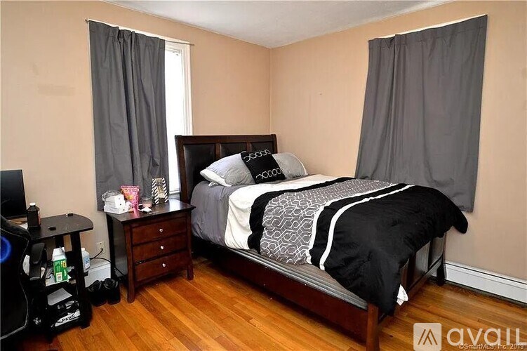 A bedroom with a bed, nightstand, and window with curtains.