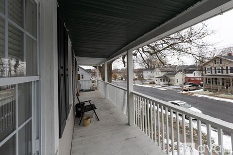 A porch with a black chair and a table with a yellow bucket on it.