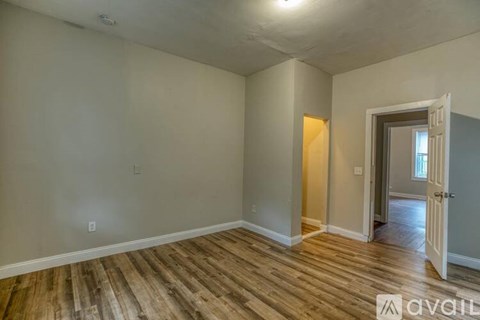 A room with wooden flooring and a door leading to another room.