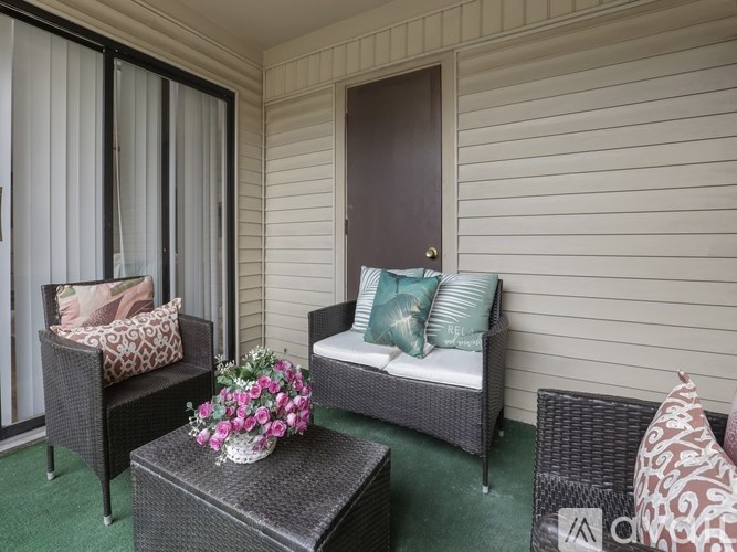 A balcony with a sofa, chair, and table with flowers.