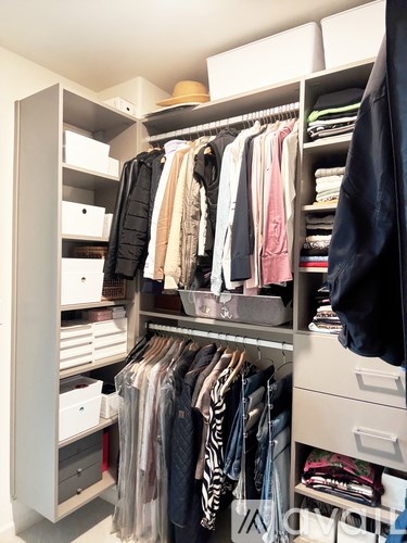 A white closet with clothes hanging and drawers underneath.