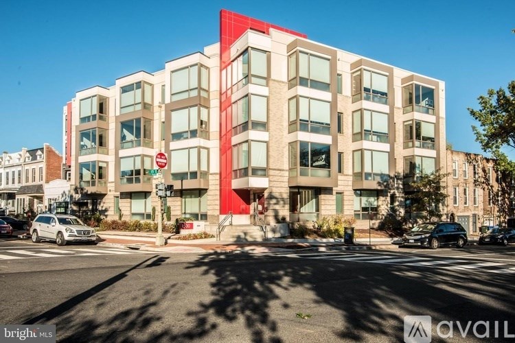 A modern building with a red accent on the side is located on a street corner.