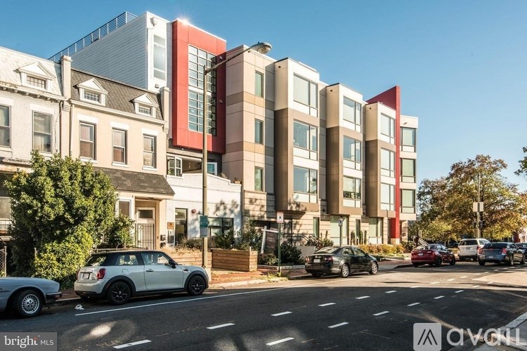 A street view of a residential area with cars parked on the side of the road and modern apartment buildings.