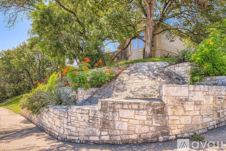 A stone retaining wall with plants and flowers in front of a house.