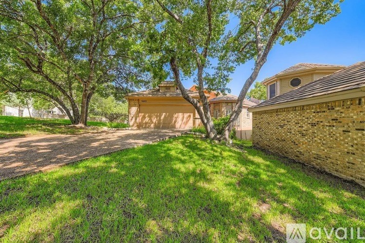A house with a brown roof and a stone wall is surrounded by trees.