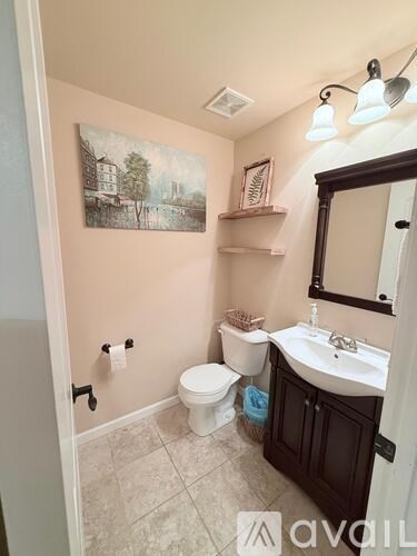 A bathroom with a toilet, sink, and a painting on the wall.