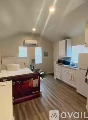 A bedroom with a bed, a TV, and a kitchen area.