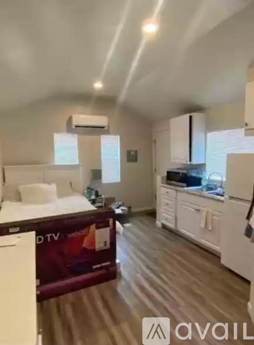 A bedroom with a bed, a TV, and a kitchen area.